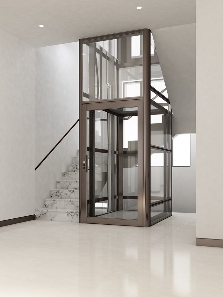 Home lift with a hinged swing door in a bronze-framed glass shaft beside a marble staircase