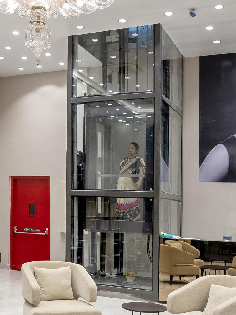 Glass-enclosed lift in a lobby with armchairs