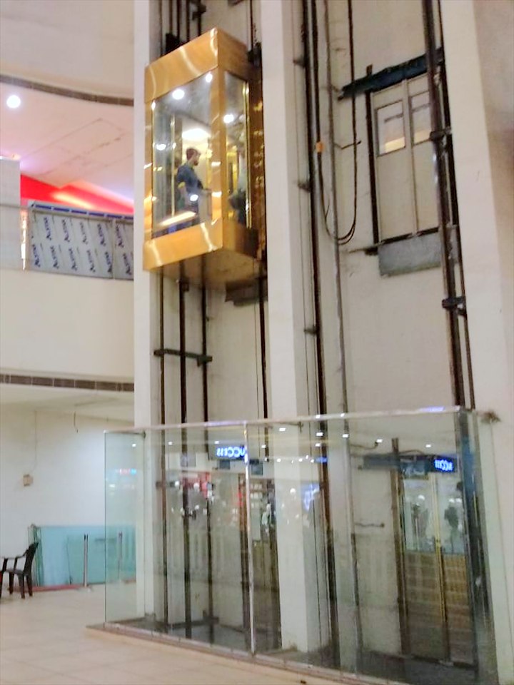 L.T. Elevator gold-framed panoramic glass lift rising through a shopping-mall atrium in Dhanbad, Jharkhand