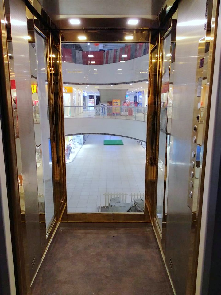Inside the panoramic car: gold-framed glass walls opening onto the mall atrium